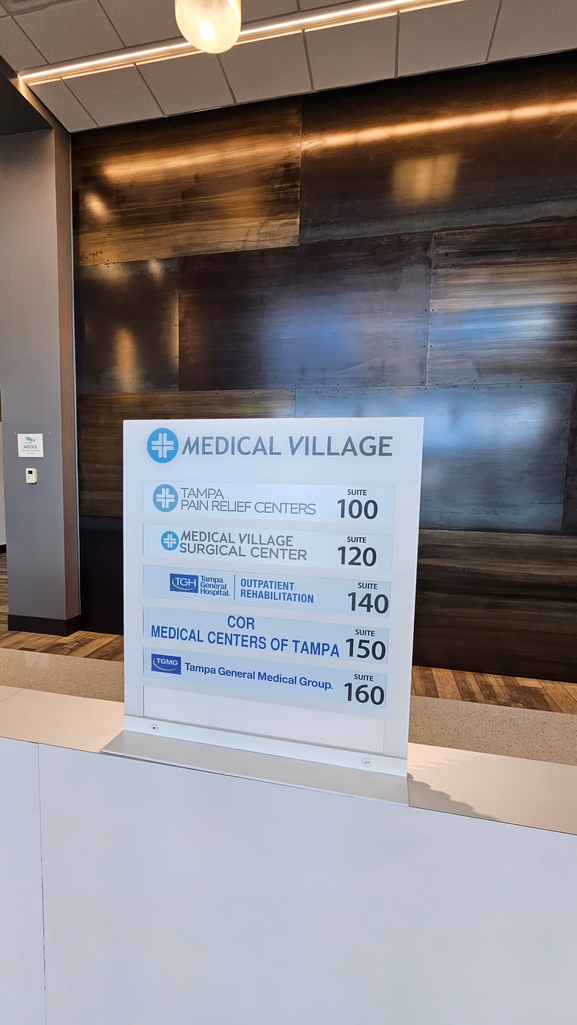 Lobby area featuring a large medical services directory sign in front of a dark wood wall.