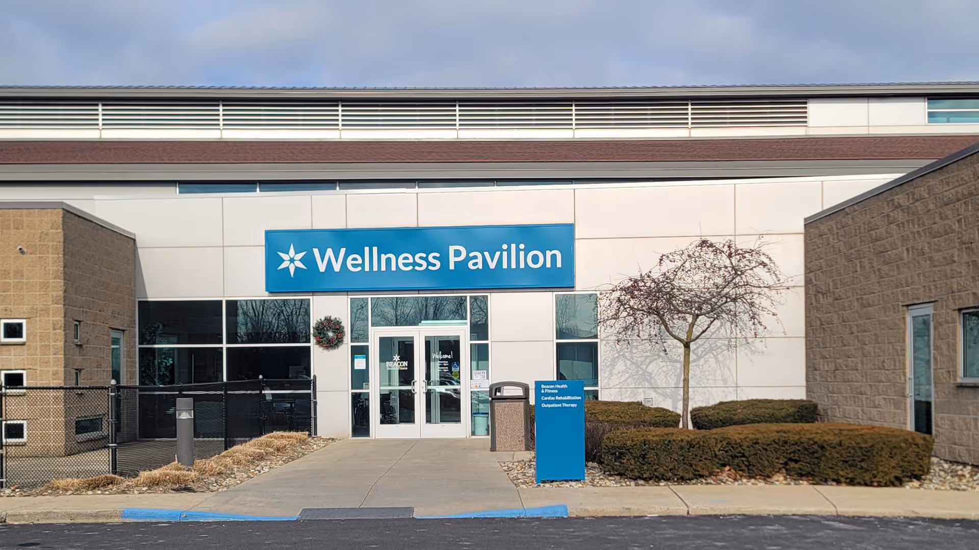Front view of a modern medical building with a blue Wellness Pavilion sign and entrance doors.