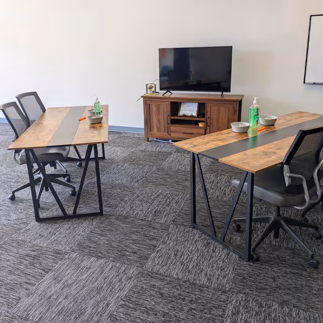 Two desks with chairs and a TV stand are arranged in a meeting room.