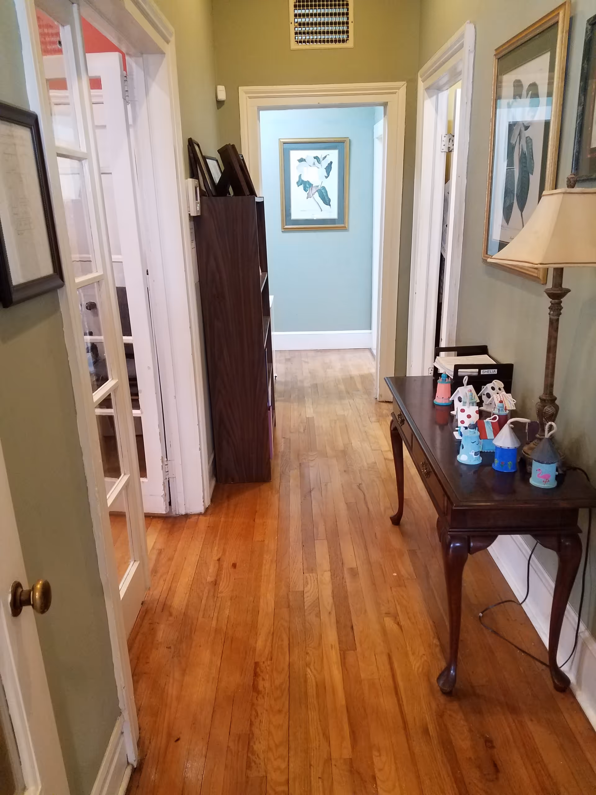 Narrow hallway in a senior care facility with wooden floors and framed art.
