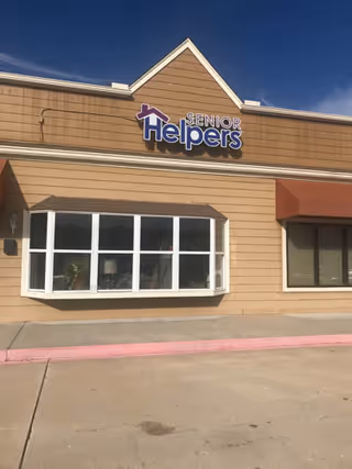 The exterior of a Senior Helpers facility with a tan facade and a large sign.