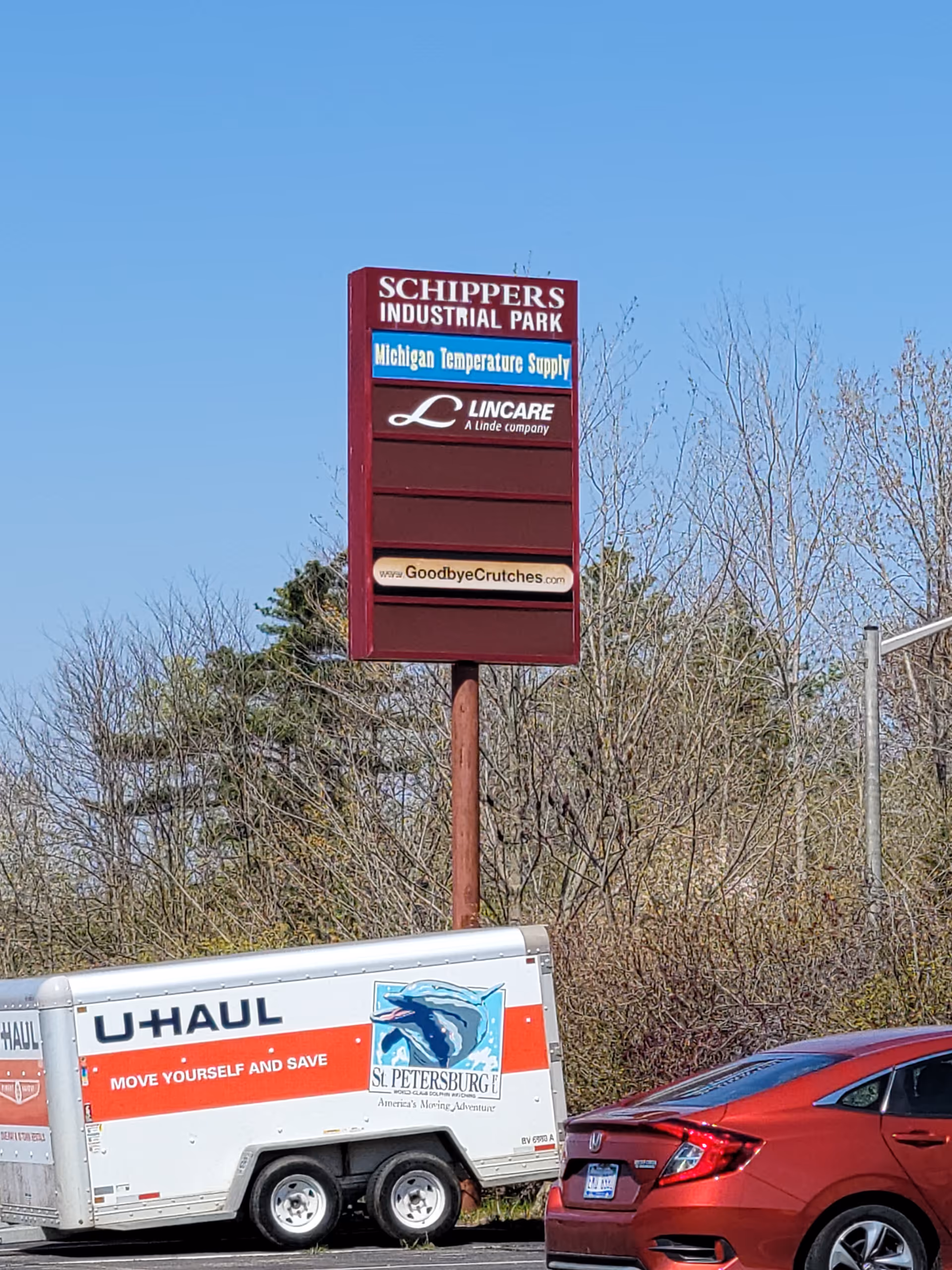 Tall maroon signboard for Lincare, with U-Haul trailer and red car nearby.