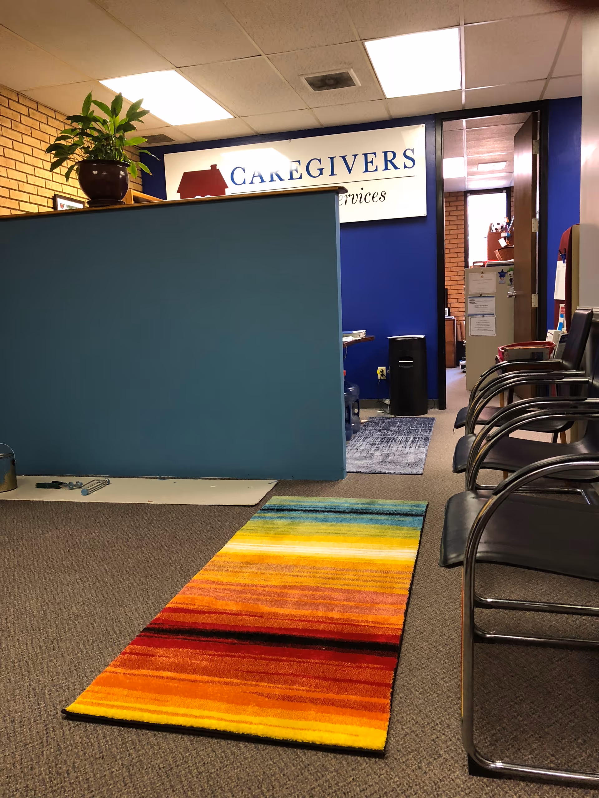 Interior of Caregivers in Home Services lobby with blue divider, rainbow rug, and chairs.