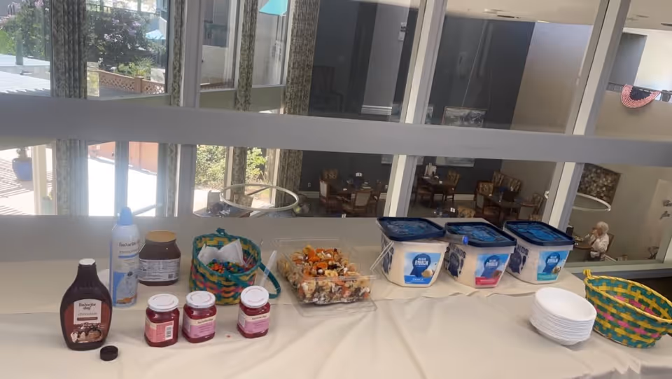 A long buffet table displays condiments, baskets, and yogurt tubs beside a dining area.