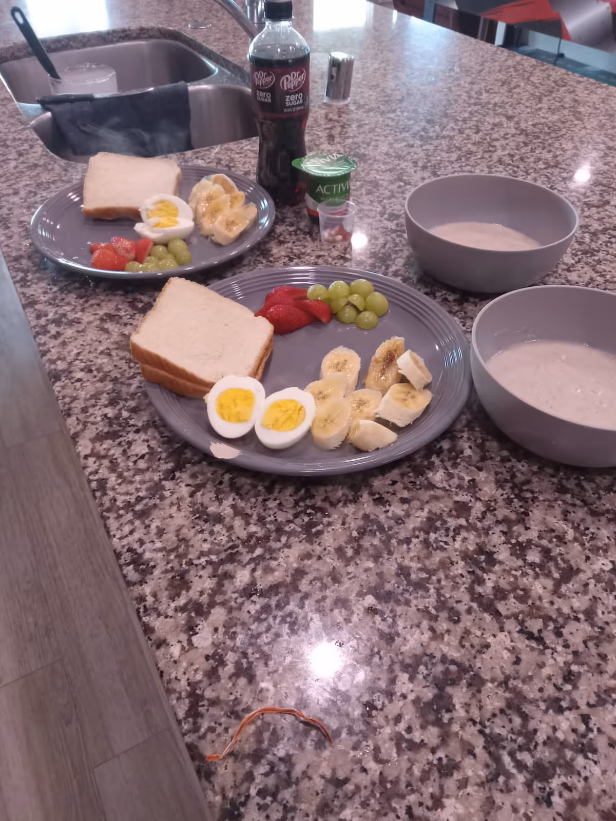Two breakfast plates with eggs, bread, fruit on a granite kitchen counter.