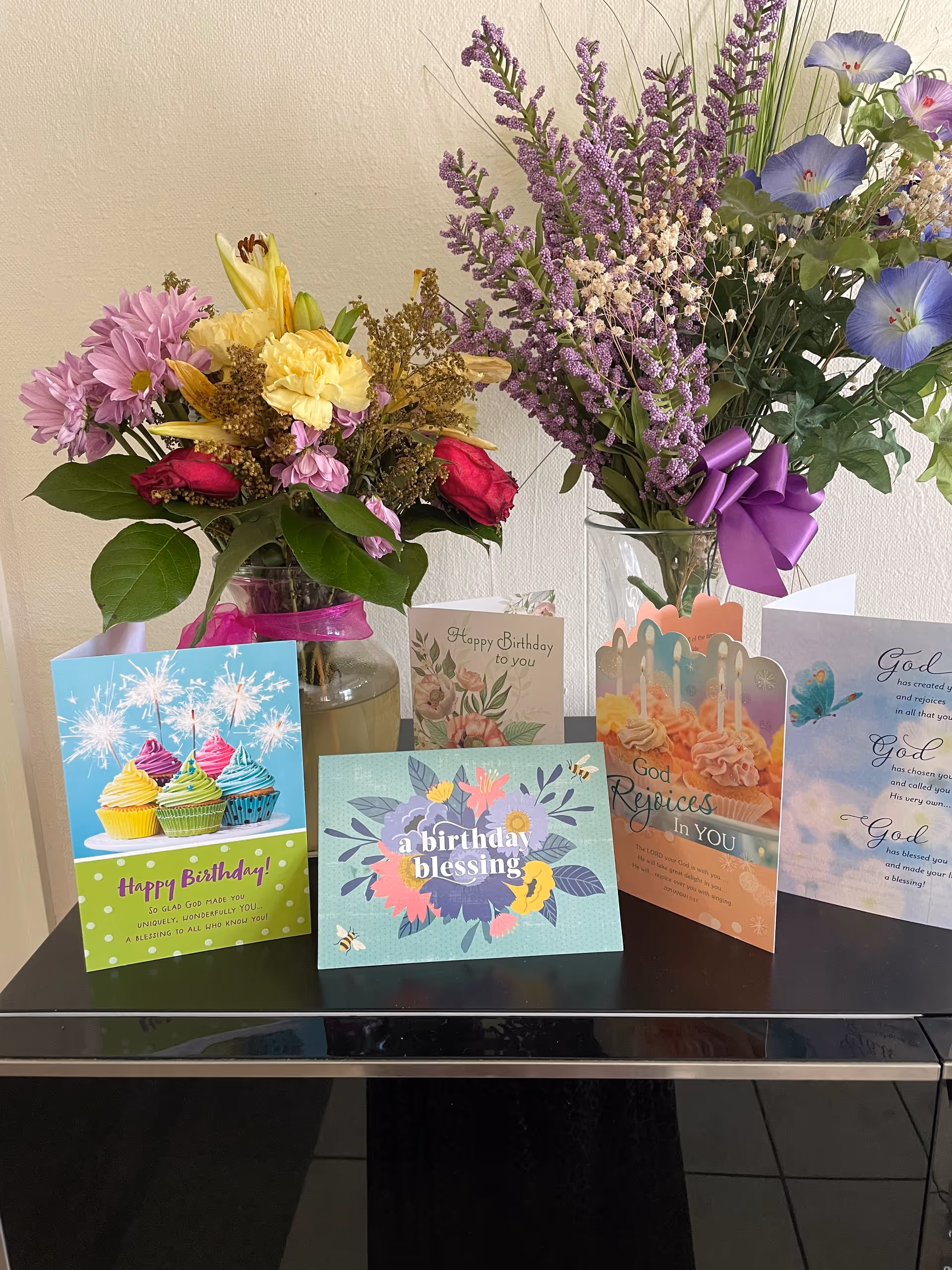 Vibrant flower arrangements and birthday cards displayed on a glossy black table indoors.