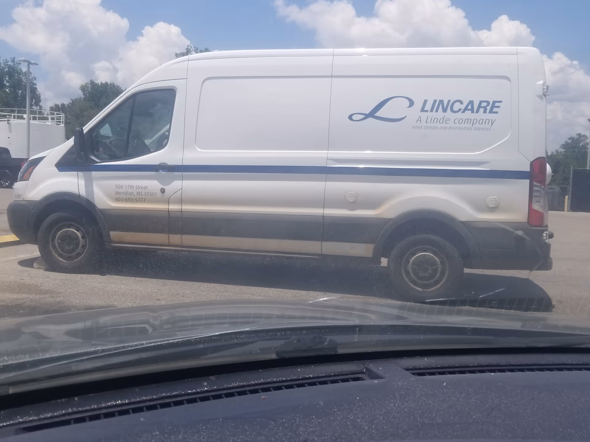 White LinCare van with blue stripe parked in a lot under a cloudy sky.