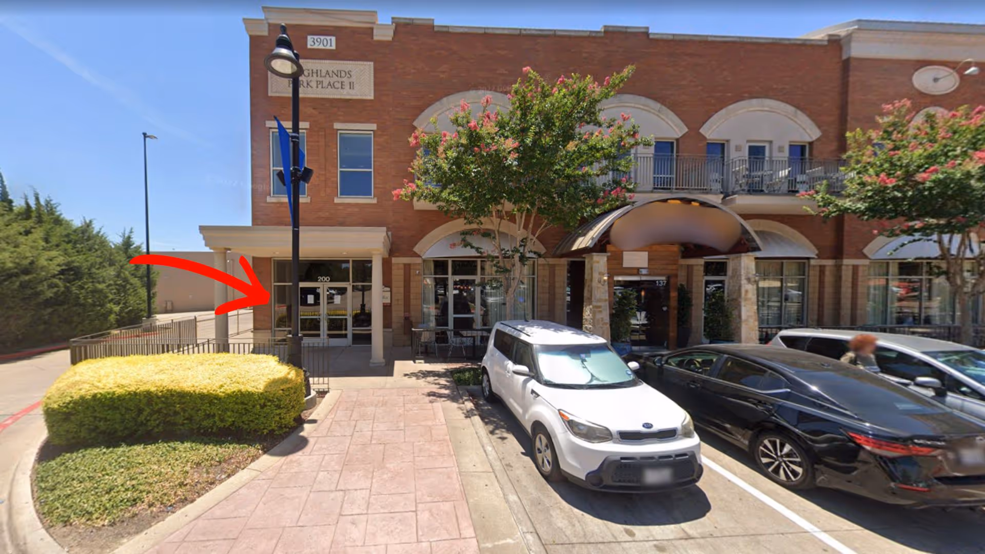Exterior view of a brick senior care facility with parked cars and landscaping.