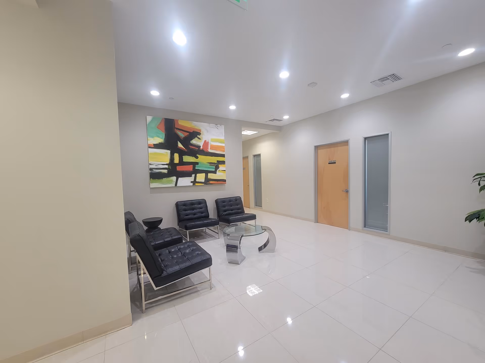 Modern lobby area with black lounge chairs, glass coffee table, and abstract art.