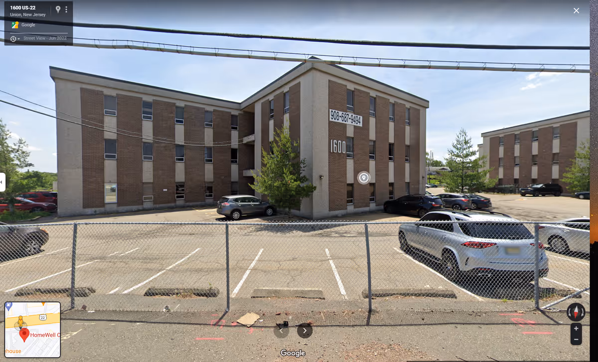 Exterior view of a brick senior care building with a parking lot and fence
