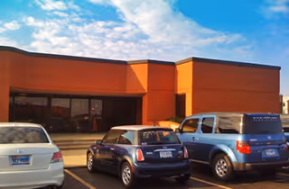 Brick building exterior with large glass front and several parked cars.