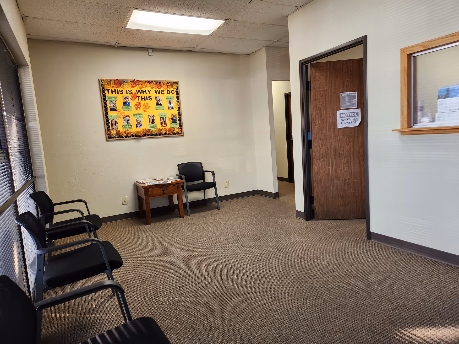 A quiet waiting area with black chairs, a bulletin board, and a wooden door.