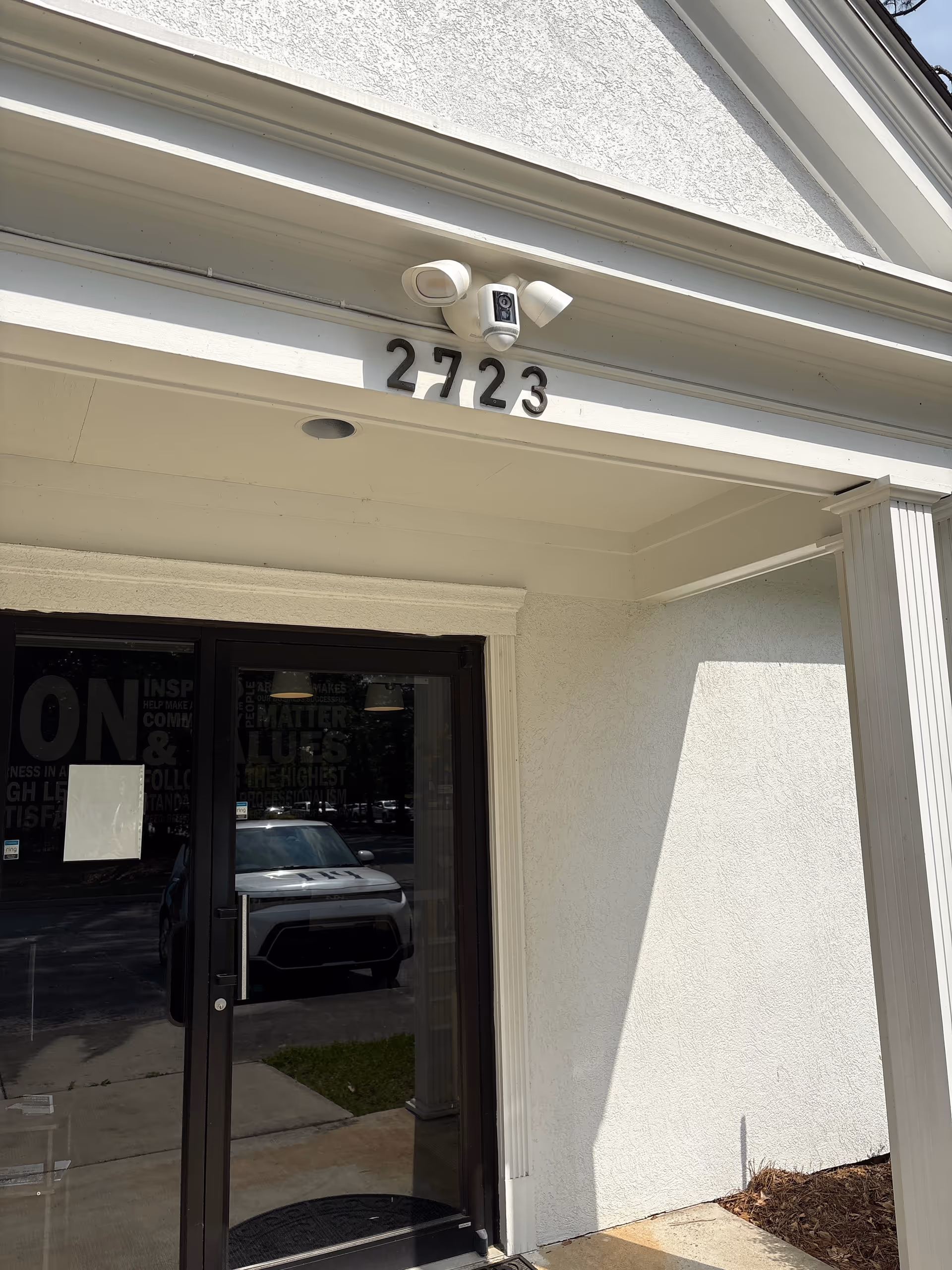 White building entrance with address 2723 and a security camera above glass doors