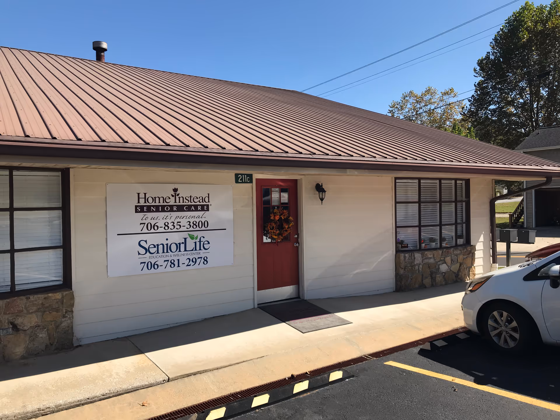 Front exterior of senior care facility with red door, signage, and parked car.