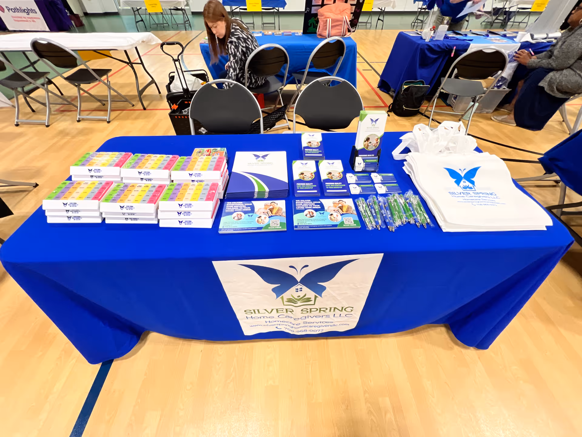 Blue table with promotional materials for Silver Spring Home Caregivers LLC at event.