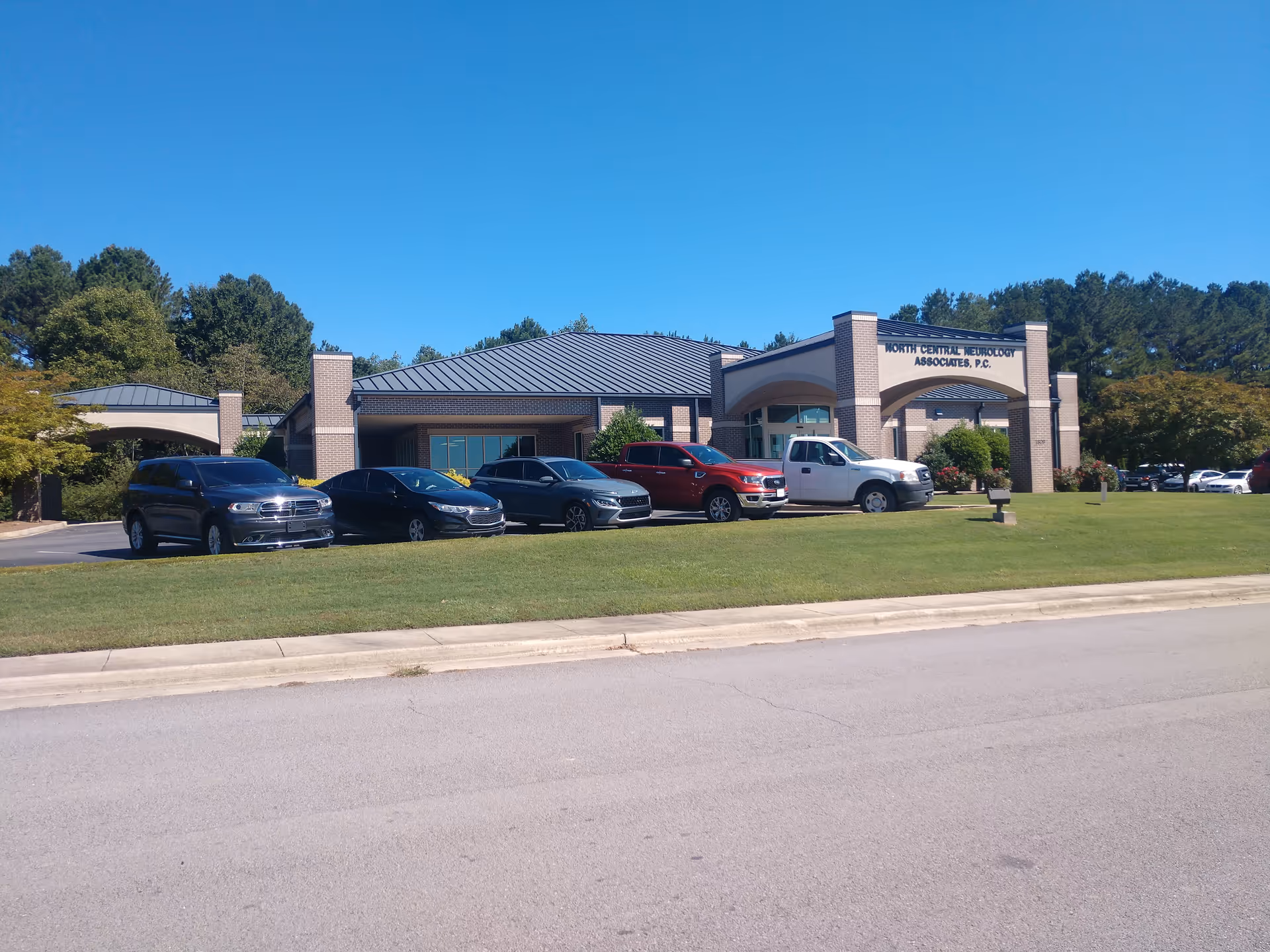 A medical center building with brick arches and a parking lot under a clear blue sky.