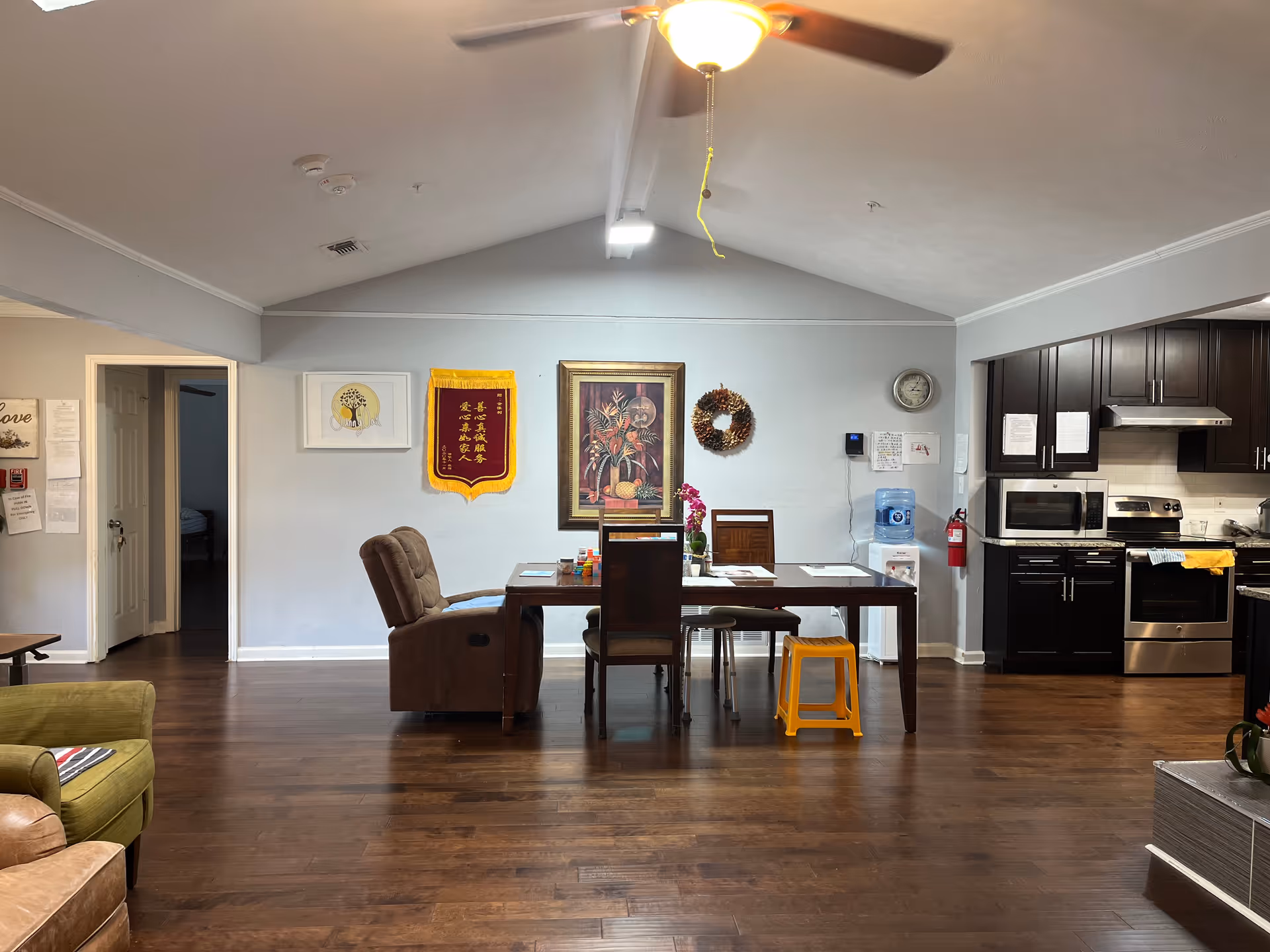 Indoor communal living area with a dining table, chairs, a recliner, and a dark kitchen.