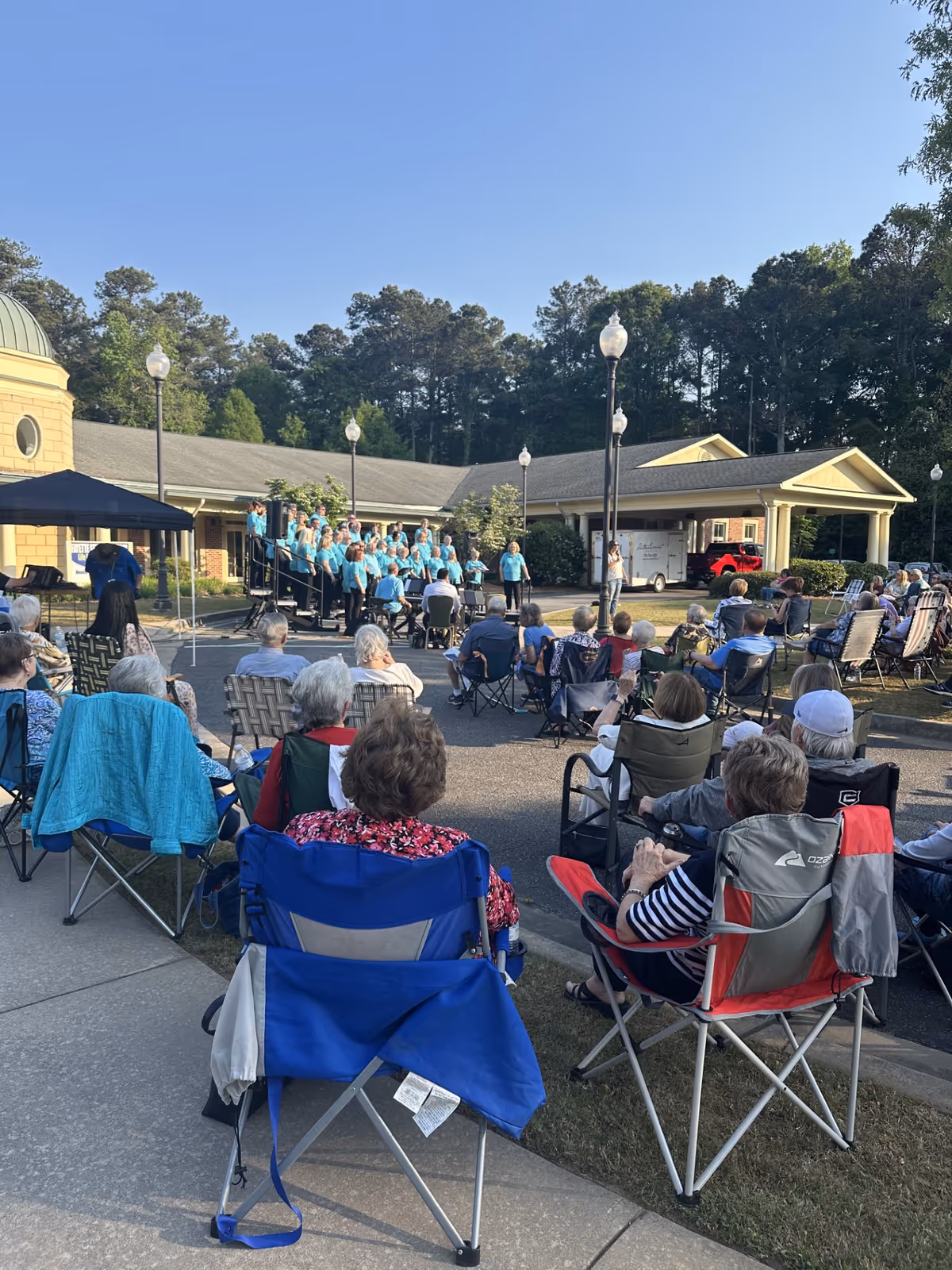 Outdoor senior living audience watches a teal-clad choir perform.