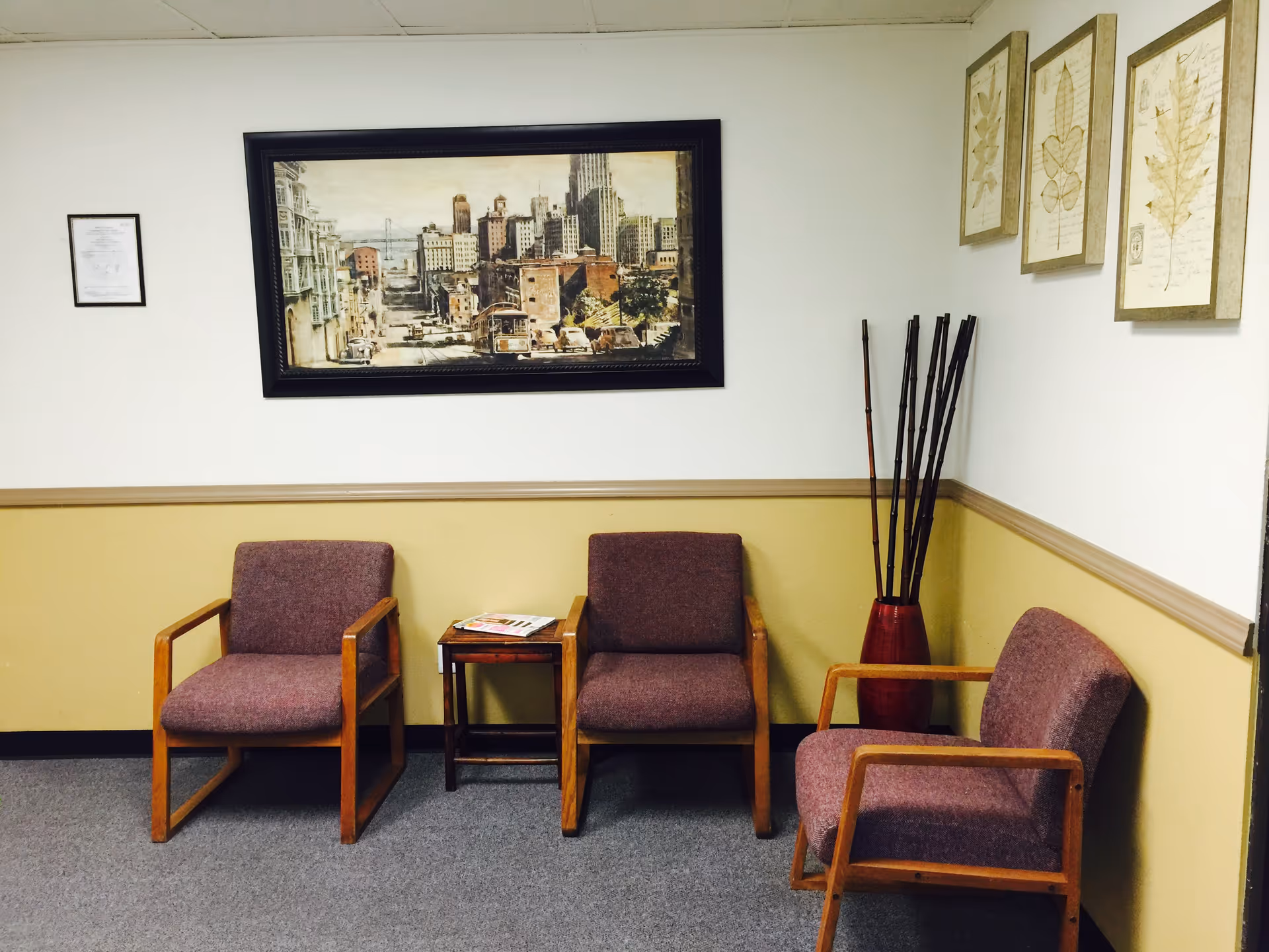 Waiting area with four purple chairs, a small table, magazines, and framed wall art.