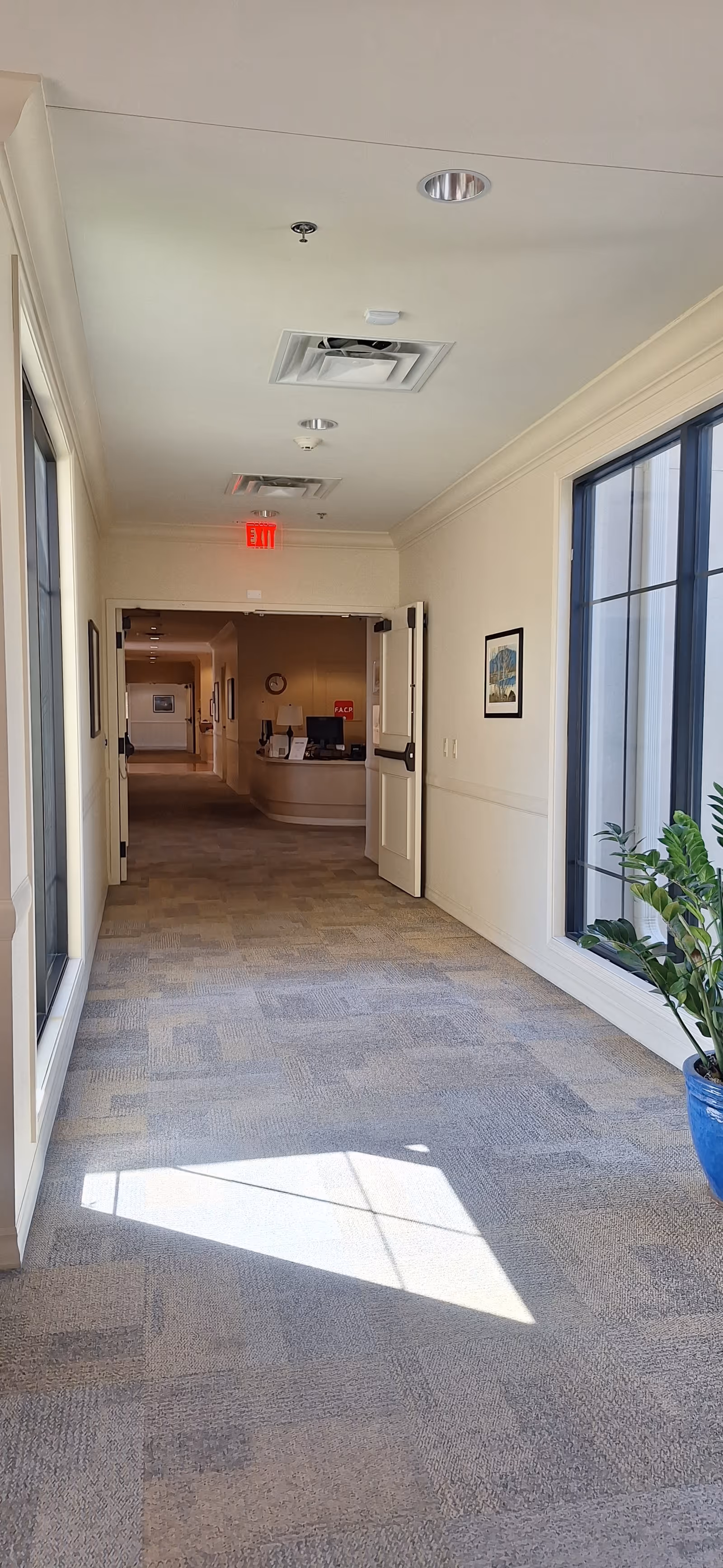Bright interior hallway of a senior living facility with windows and a distant reception.