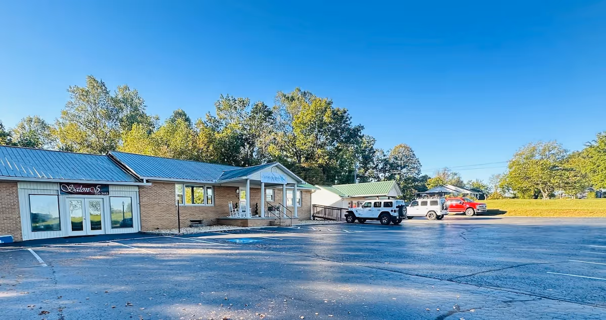 Exterior view of a single-story senior care facility with a parking lot and vans.