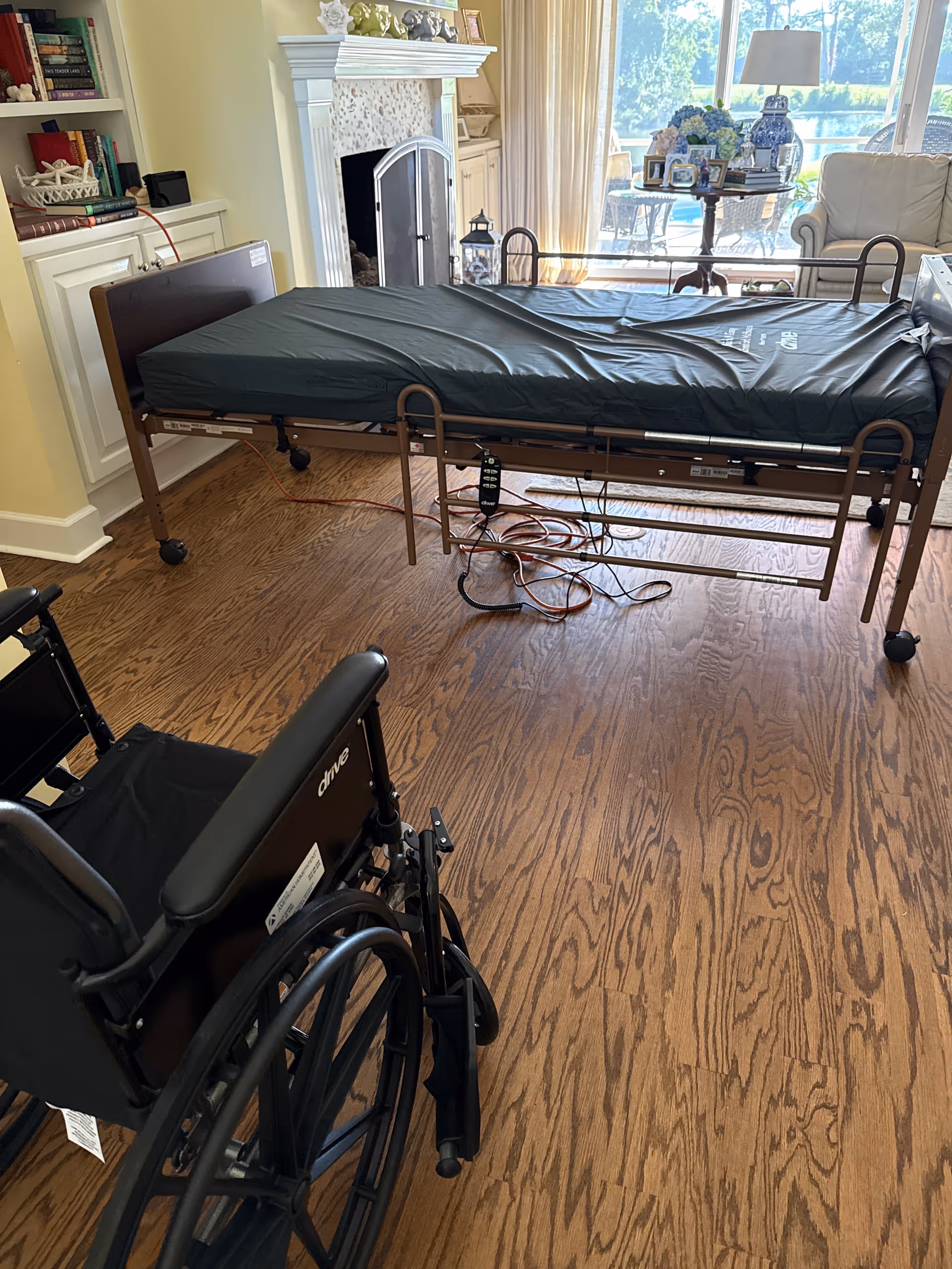 A hospital bed and wheelchair in a sunny, well-furnished senior living room.