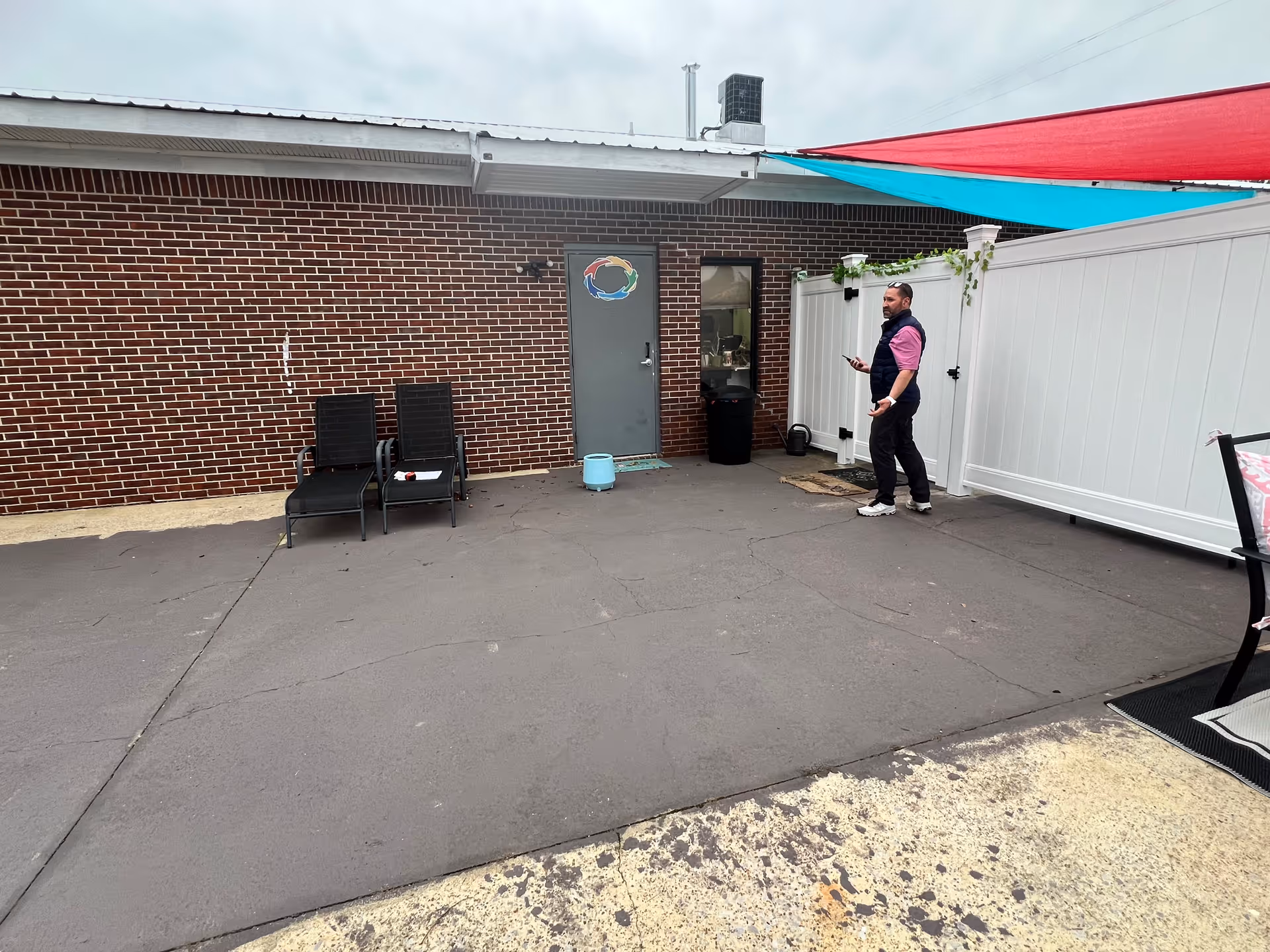 A staff member stands outside a brick building with chairs and a blue bucket.