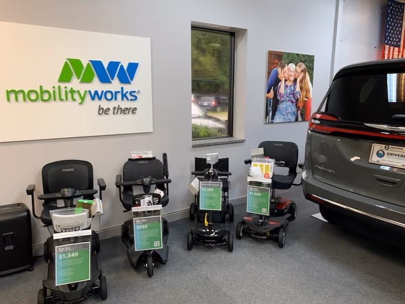 Inside a MobilityWorks showroom, multiple mobility scooters are displayed next to a parked SUV.