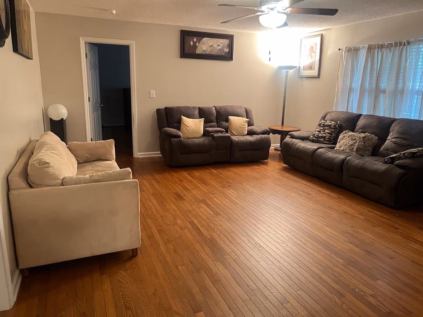 Spacious living room with beige and dark leather sofas, wood floor, and a floor lamp.