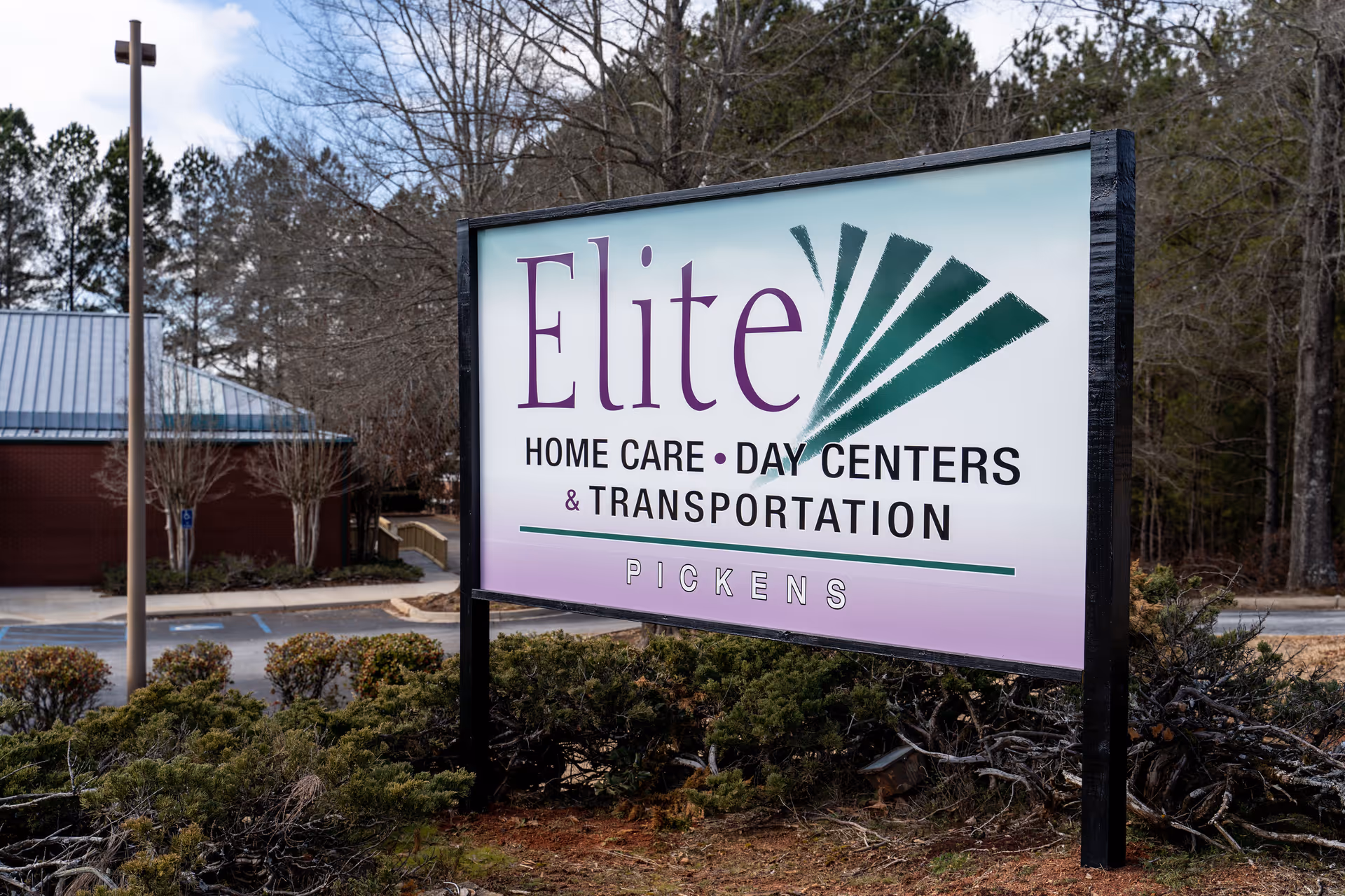 An outdoor sign reads Elite Home Care, Day Centers and Transportation near trees.