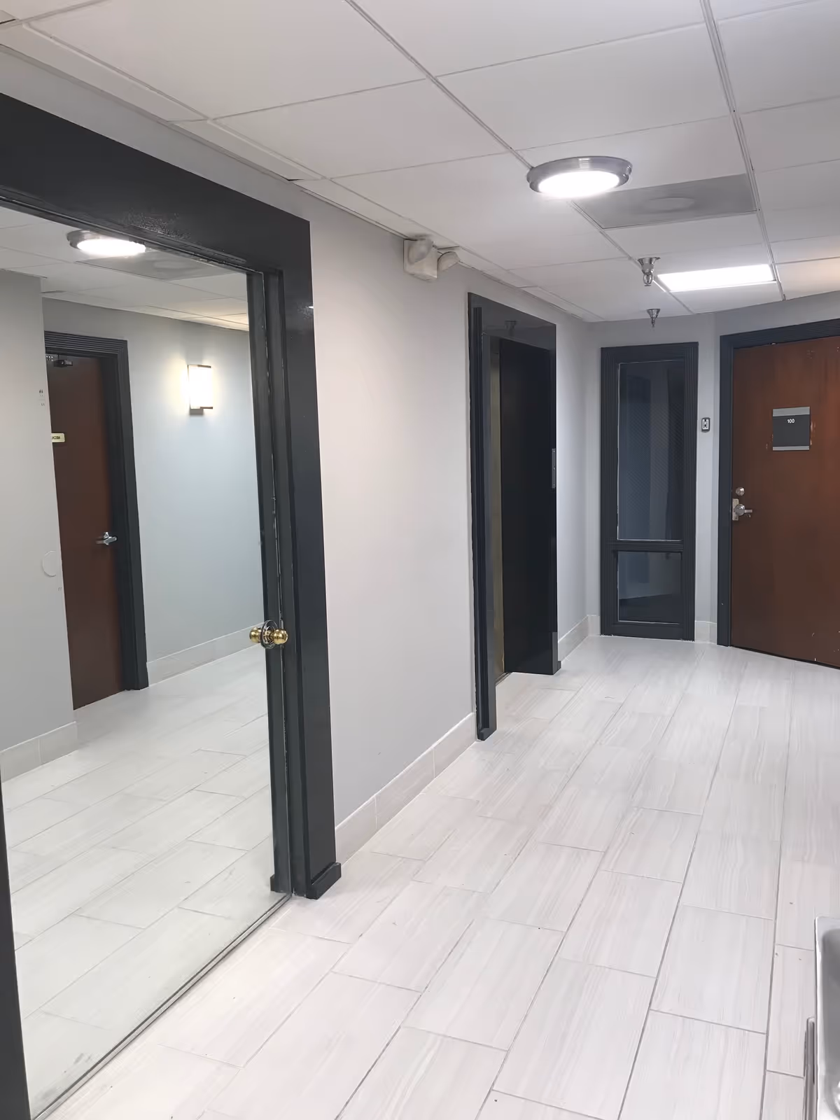 Well-lit hallway with multiple doors and a mirrored wall in a senior living facility.