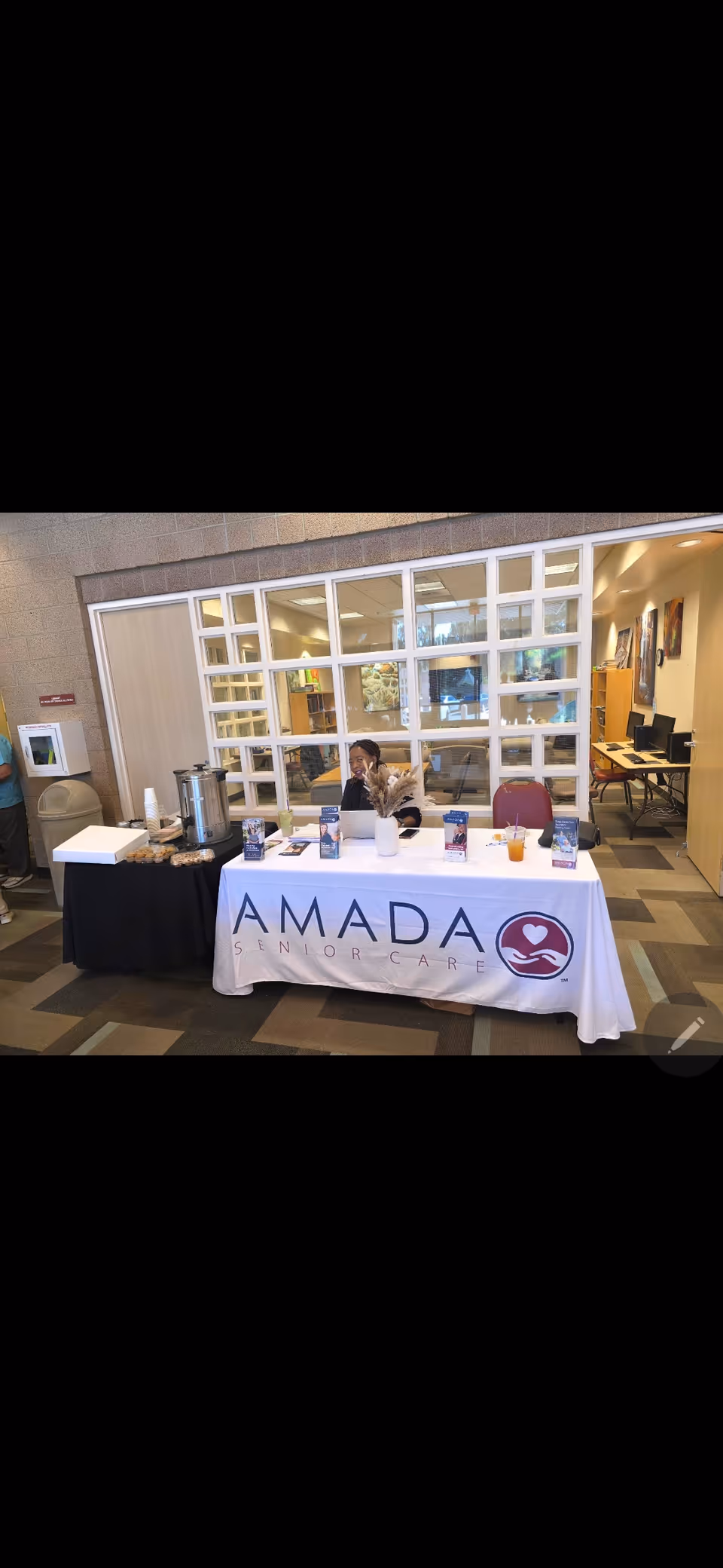 Promotional Amada Senior Care table set up in a lobby with glass partition walls