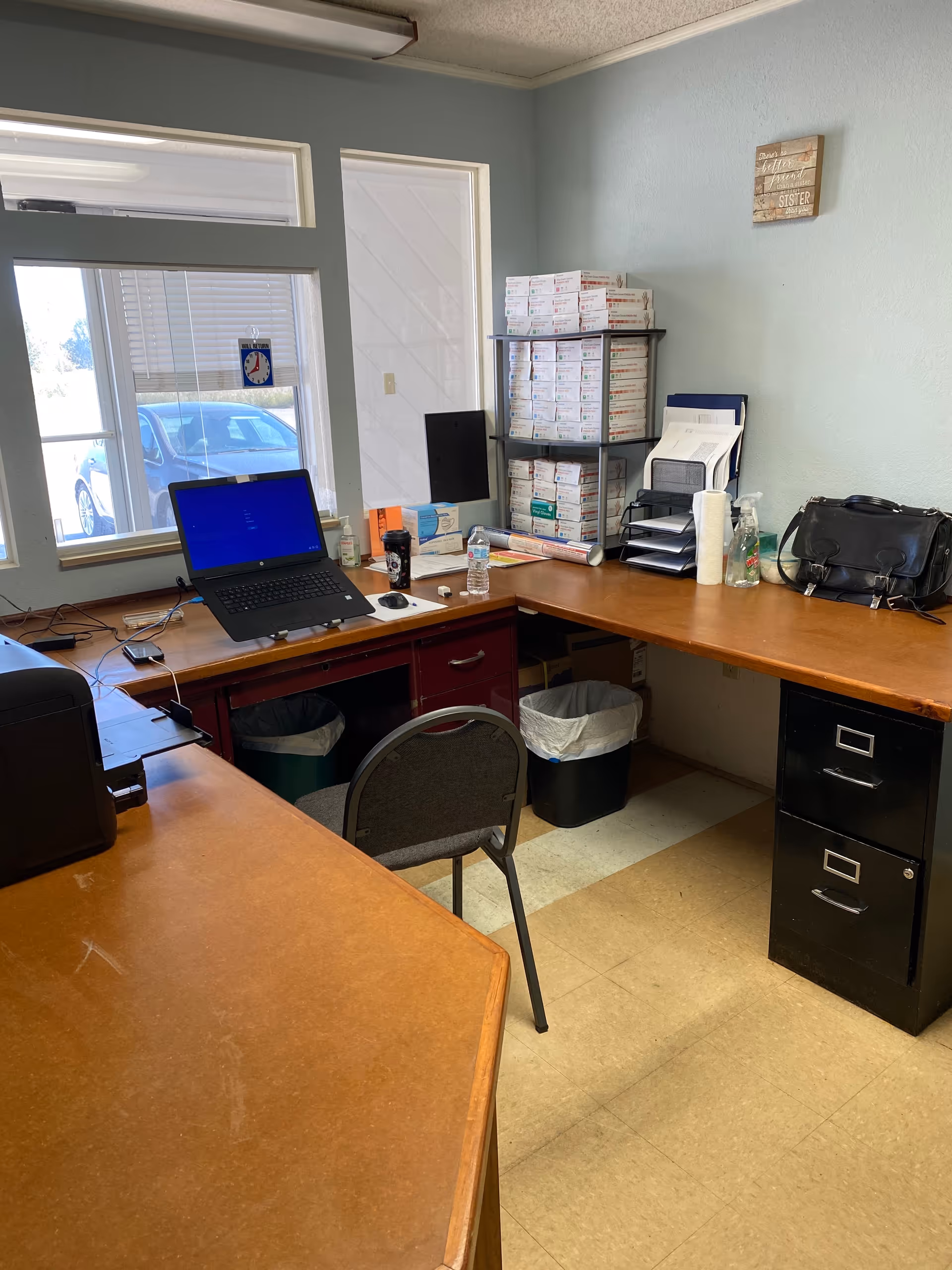 Office workspace featuring a laptop, printer, stacked boxes, shelves, and a filing cabinet.