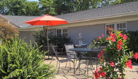 Outdoor patio of a Holiday Health Care facility with a table, chairs, and red umbrella.