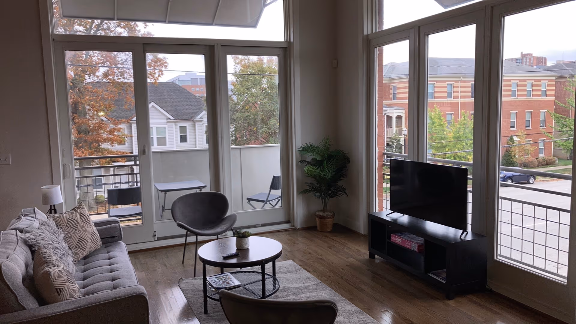 Bright living room with sofa, chairs, coffee table, TV, and large windows.