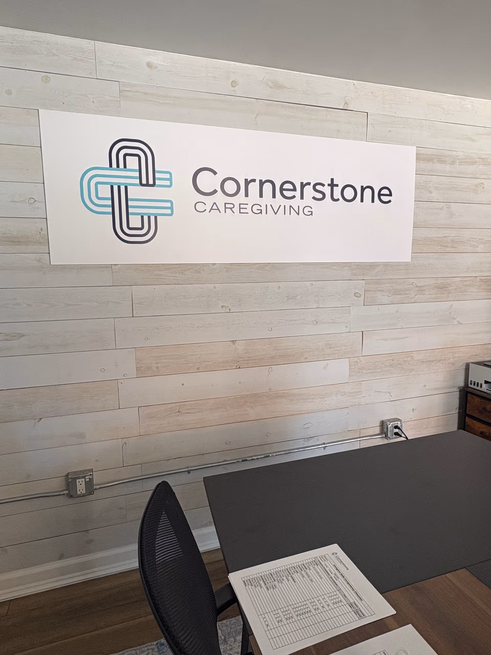 Reception desk in an interior space with a Cornerstone Caregiving sign on a light wood wall.