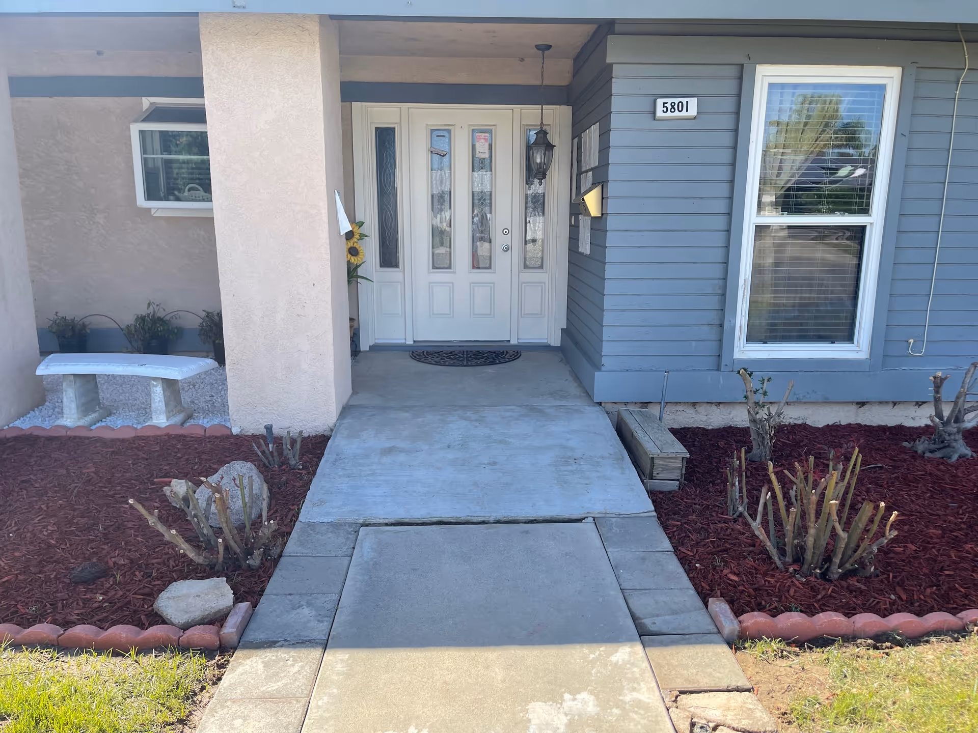 Front entrance of a home care facility with white doors, walkway, and landscaping.