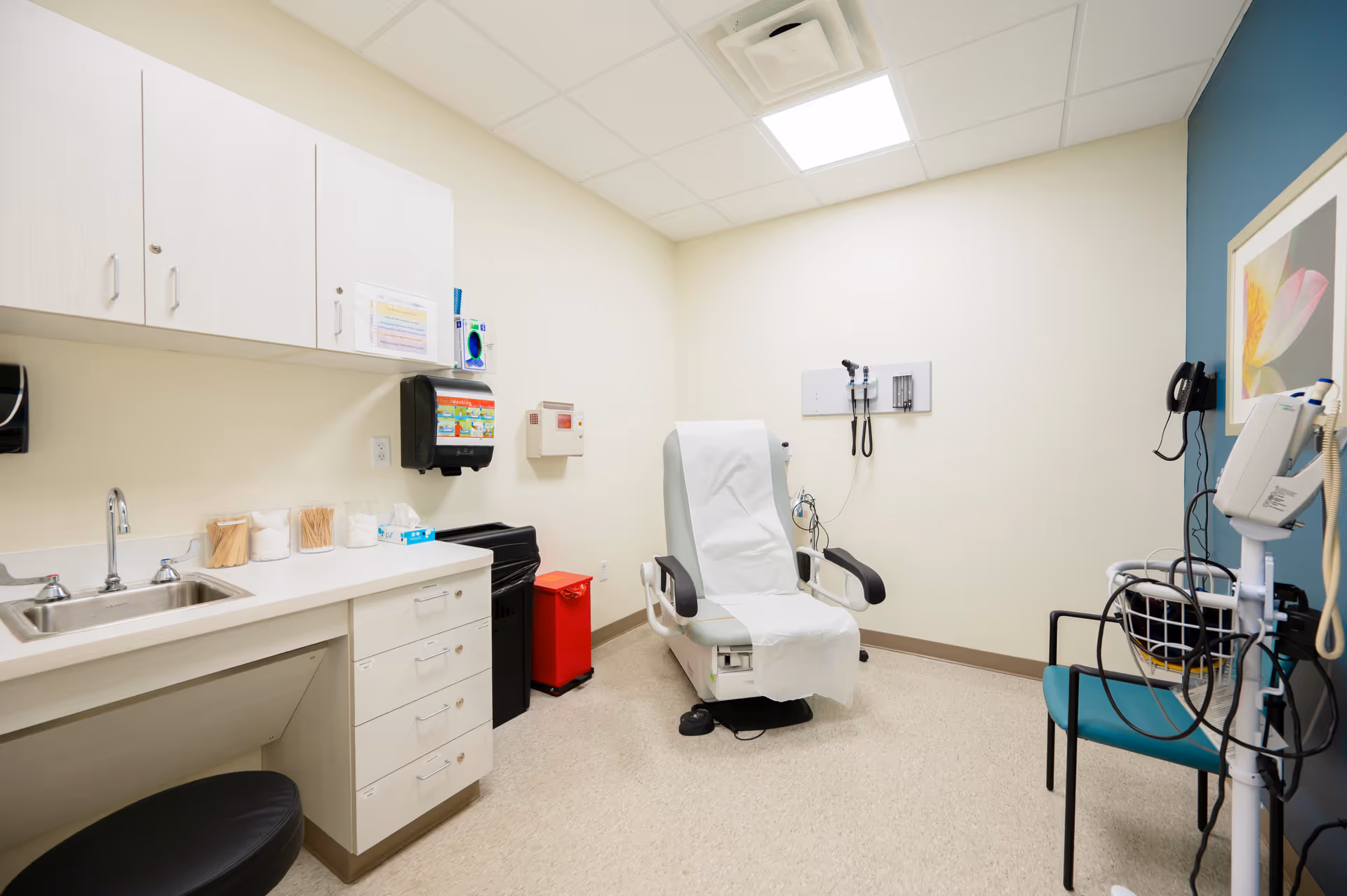 Empty medical examination room with a reclining chair, sink, cabinets, and medical equipment.