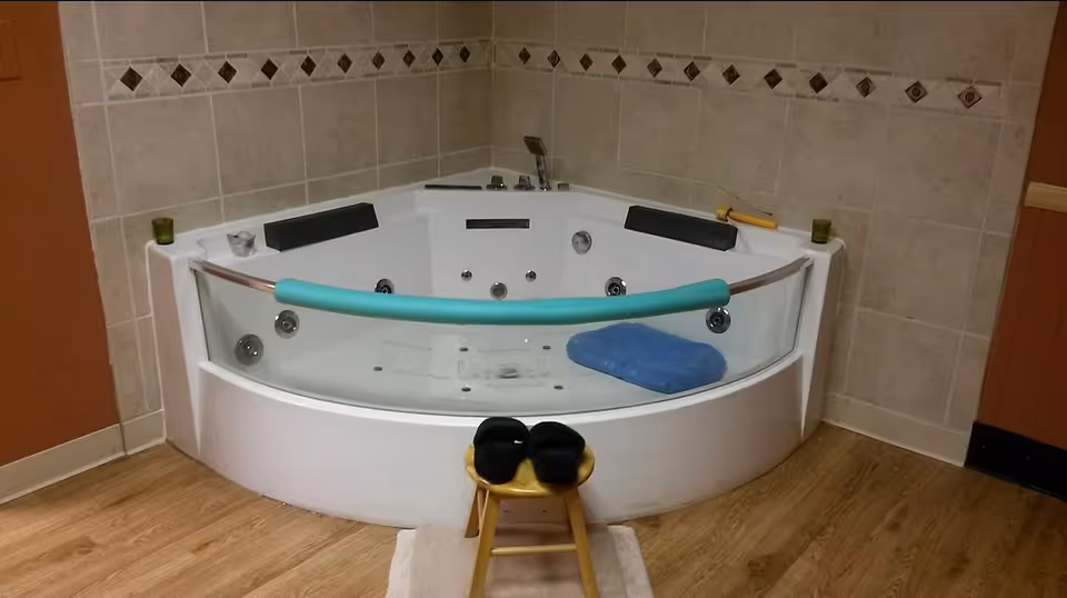 A spacious bathroom with a large white jacuzzi tub, beige tiled walls, and a wooden floor.