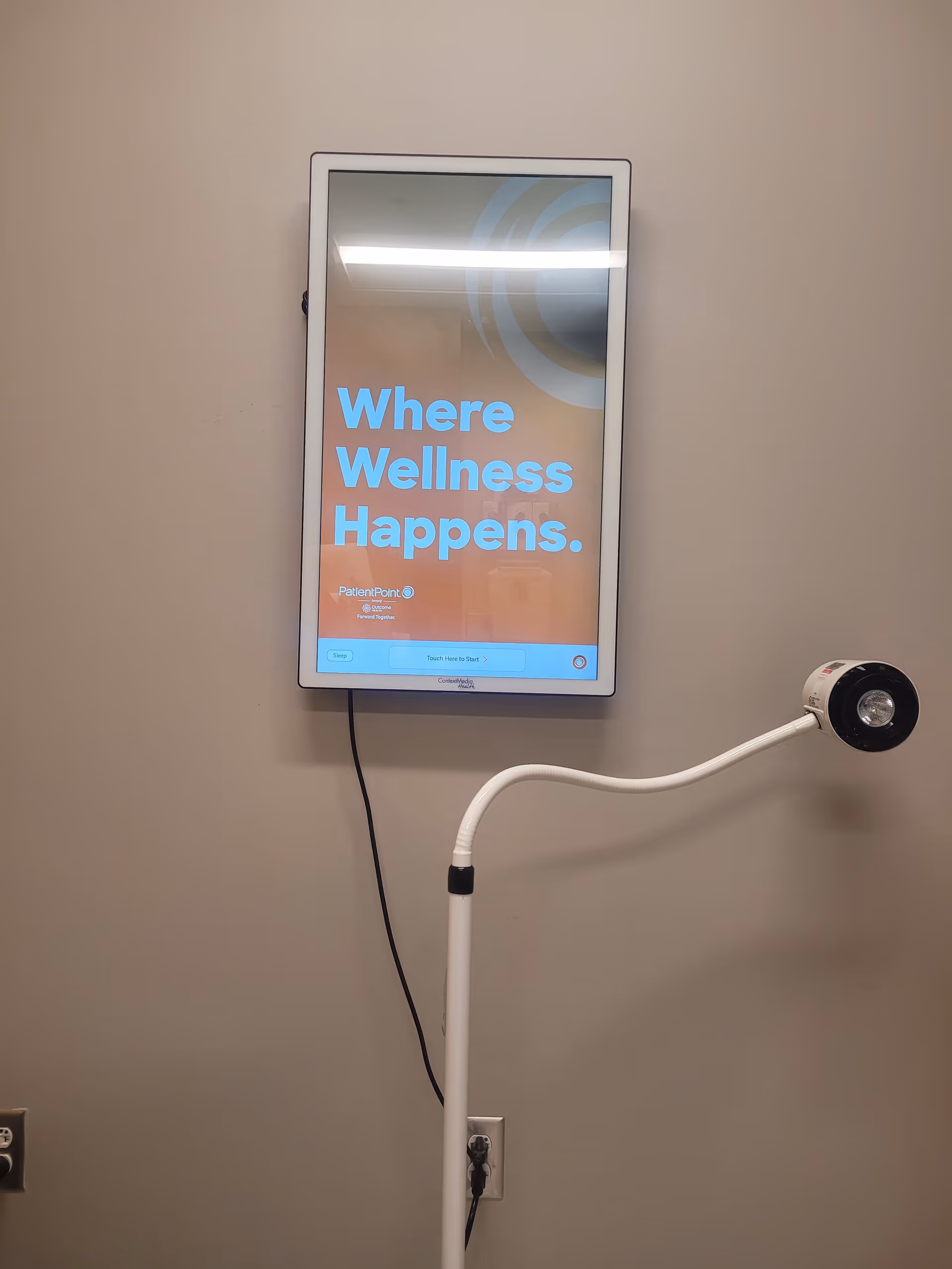 Wall-mounted digital sign displaying 'Where Wellness Happens' in a clinical hallway.