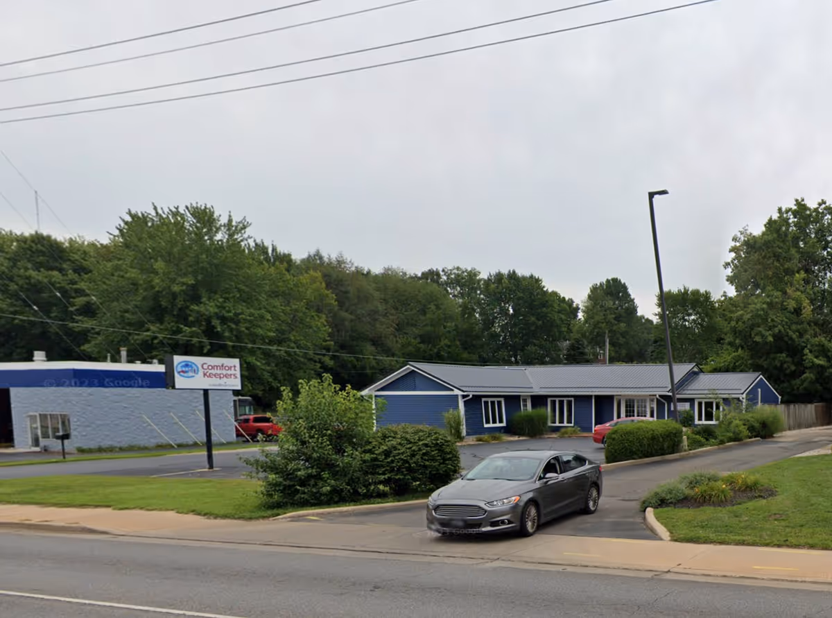 Blue single-story facility with a Comfort Keepers sign and parked cars in front