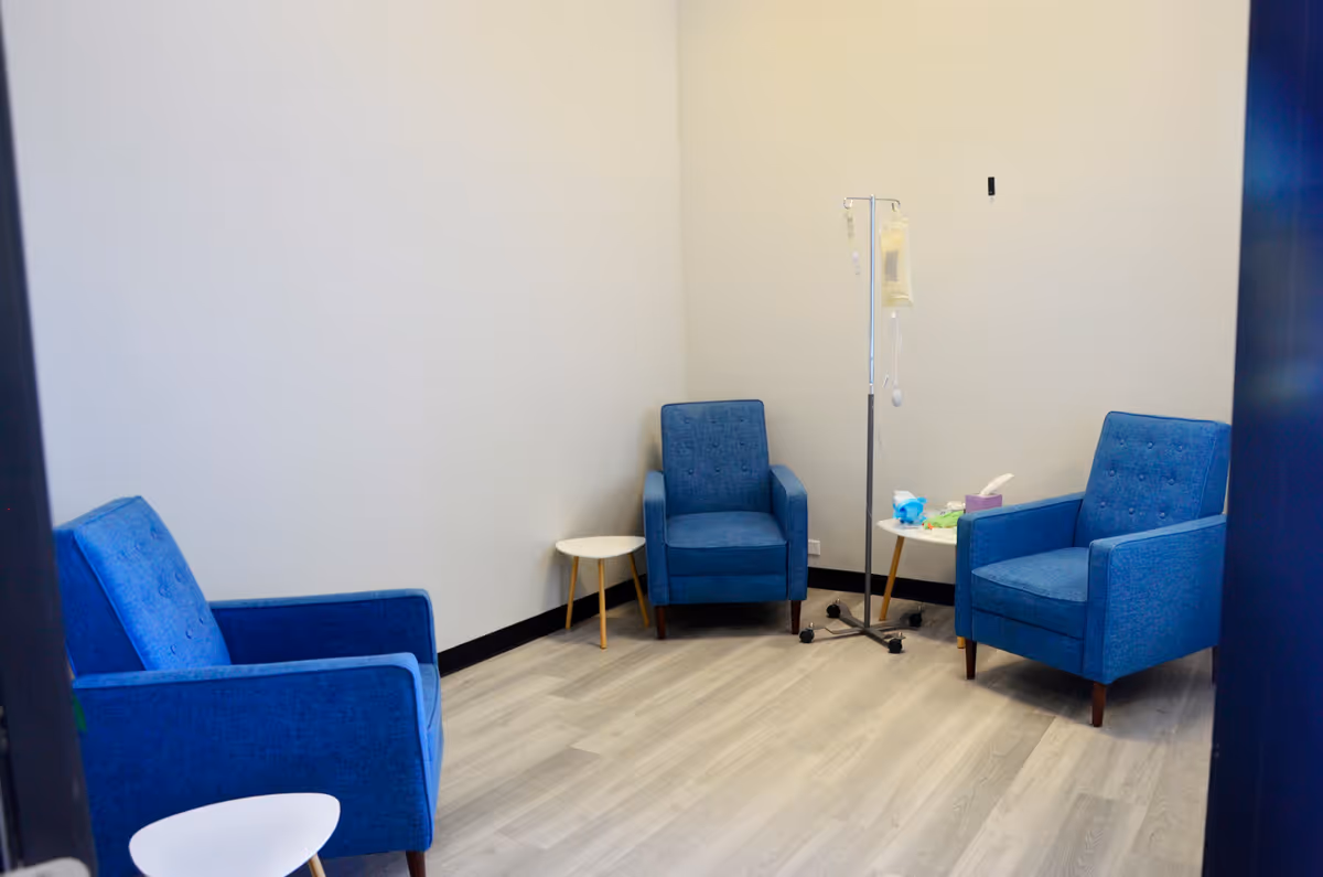 Blue chairs form a small clinic seating area with an IV pole in a bright room.