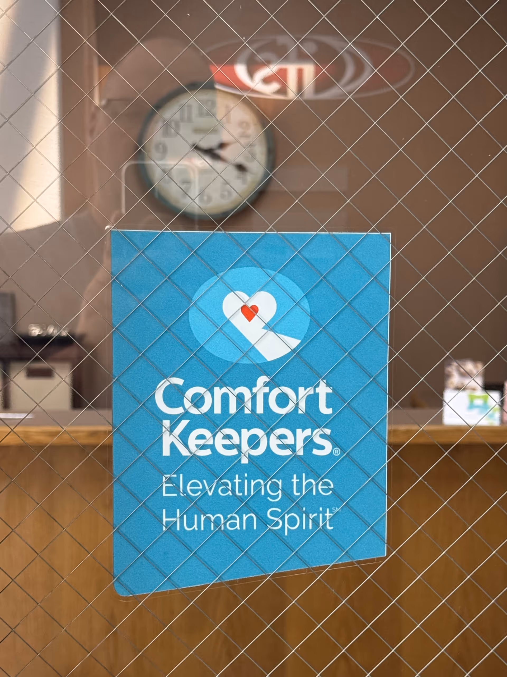 Blue Comfort Keepers sign on a wooden reception desk inside a facility.