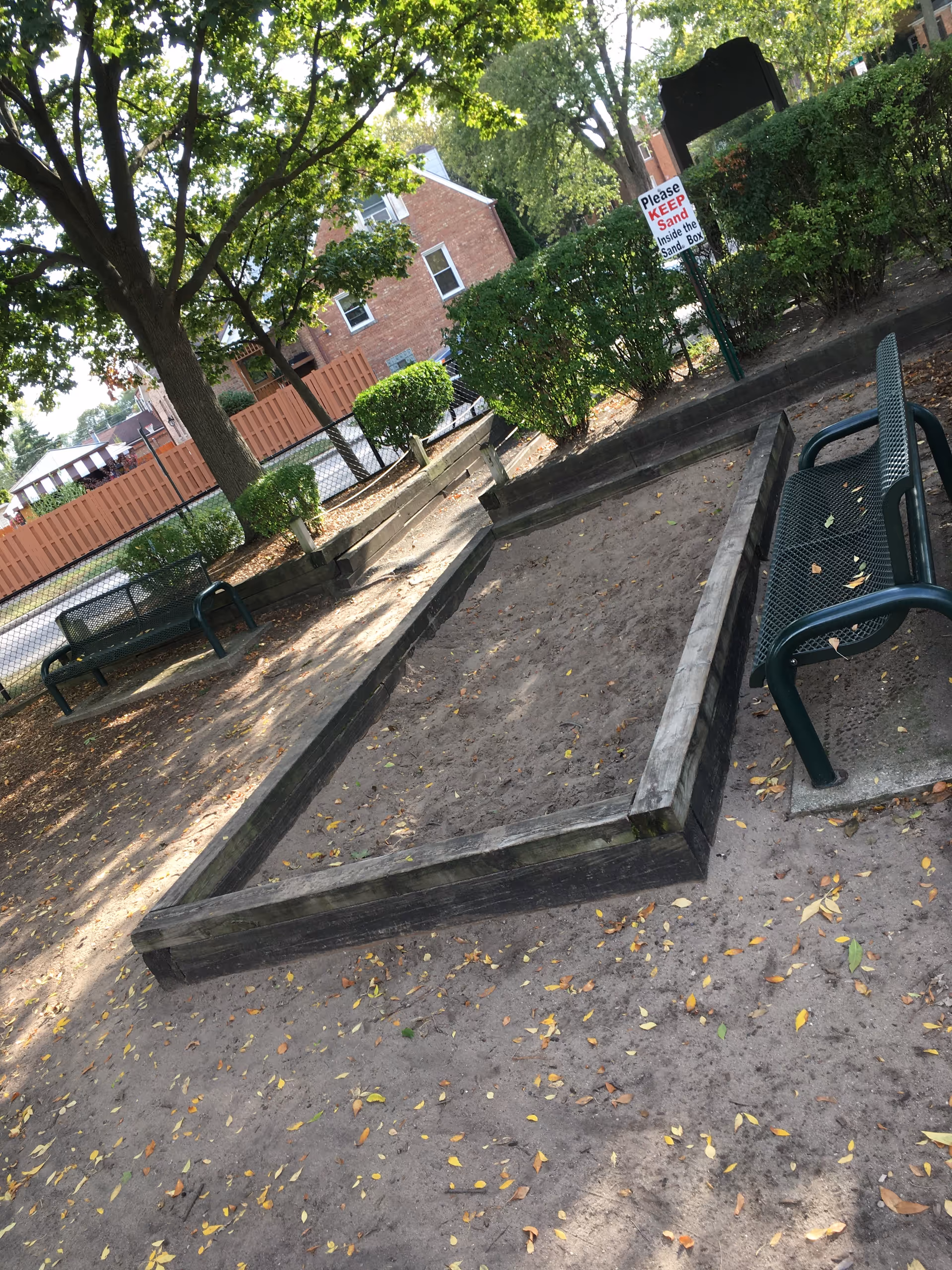 Outdoor courtyard of a senior care facility with benches, trees, planters, and a sand area.