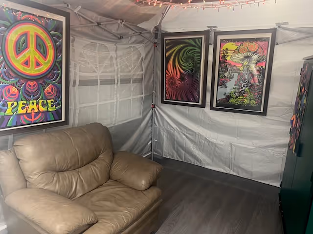 Interior tent-like room with a tan leather sofa and vibrant framed psychedelic artwork.