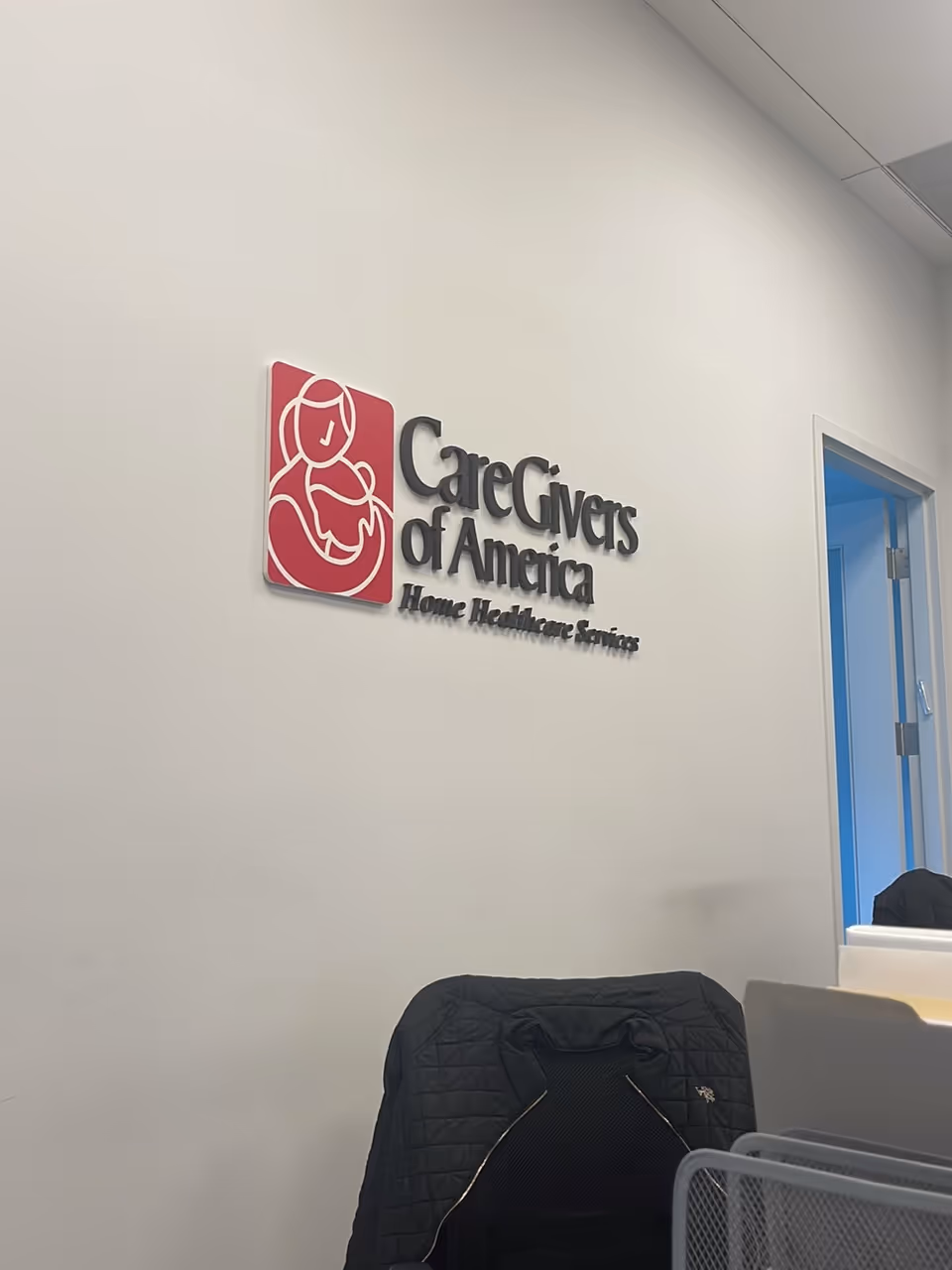 Interior office wall displaying CareGivers of America logo, with a jacket on a chair.