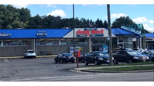 View of a Discount Drug Mart storefront with blue awnings and parked cars.