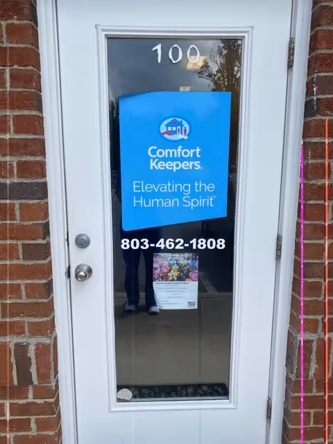 White door with blue Comfort Keepers sign and phone number on brick exterior.