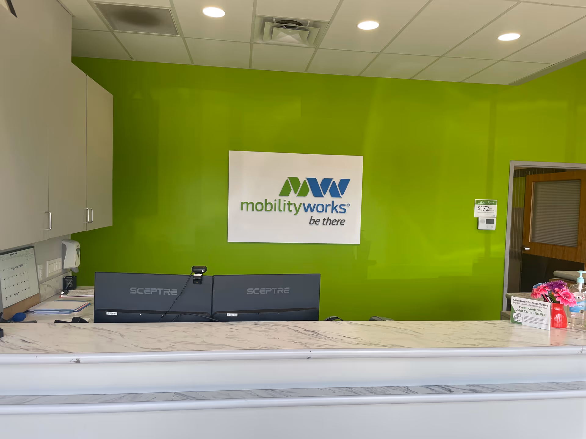 Bright green reception area with MobilityWorks sign, marble countertop, and two computer monitors.