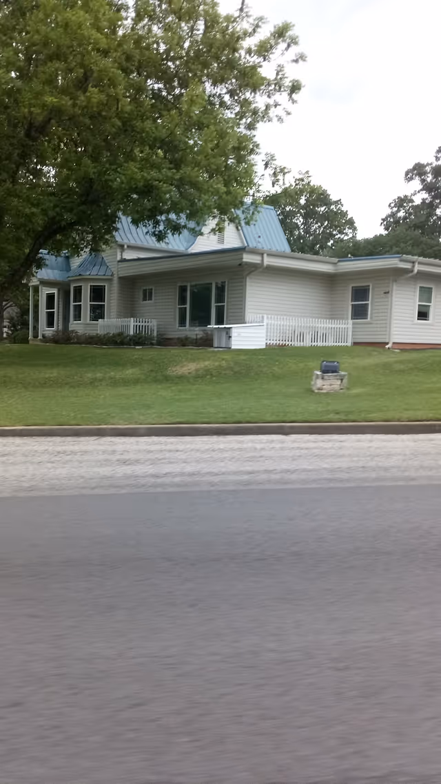 Exterior view of a single-story white building with blue roof on grassy lawn.